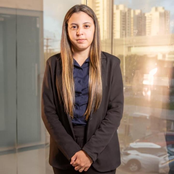 Janekelly Moreira em pé, de blazer preto, diante de uma fachada de vidro