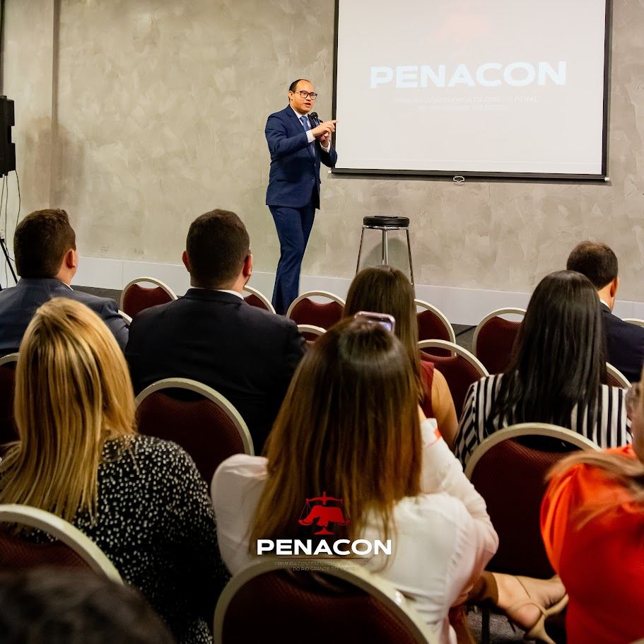 Palestrante diante do telão, com a plateia em primeiro plano, na I PENACON